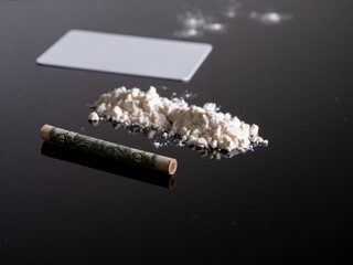 Lines of cocaine and a dollar bill. Cocaine lines shots on a black table glass. Cocaine powder, Credit card, close up, toned. Drug abuse concept. White poder on black table