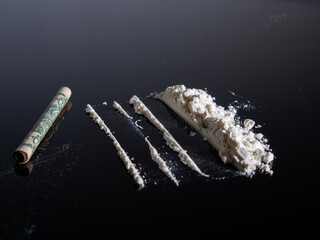 Lines of cocaine and a dollar bill. Cocaine lines shots on a black table glass. Cocaine powder,...