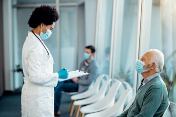 African American doctor analyzing medical report of her senior patient at medical clinic.