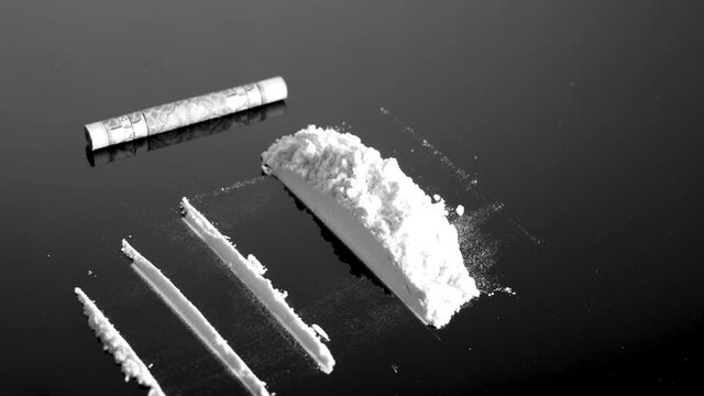 Lines of cocaine and a dollar bill. Cocaine lines shots on a black table glass. Cocaine powder, Credit card, close up, toned. Drug abuse concept. White poder on black table