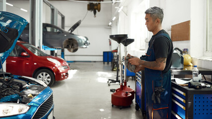 Asian man looking into open hood at car service station