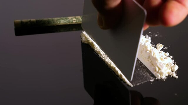 A rolled banknote snorting a line of cocaine powder. Drug Abuse. Sniffing Cocaine lines. White powder on black table. Macro shot.