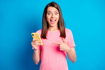 Photo portrait of female blogger pointing finger at mobile phone staring isolated on bright blue color background