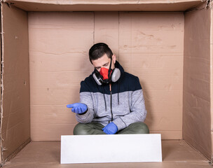  man in a protective mask sits at a cardboard box, puts out his hand, a sign of begging