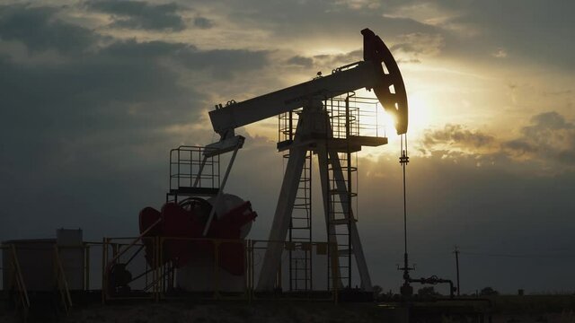 Oil mining, an oil rig in the field pumps out oil, view of an oil rig at sunset, resource extraction for fuel production, sunset light in the golden hour, timelapse.