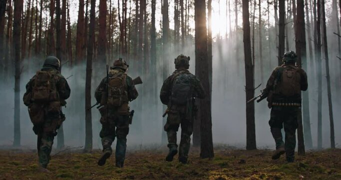 Fully Equipped Soldiers Wearing Camouflage Uniform Attacking Enemy, Rifles Ready to Shoot. Military Operation in Action, Squad walking in Formation Through Dark Dense Smokey Forest.