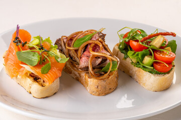 three types of bruschetta. With fish, meat, and veggie. Traditional Italian appetizers(bruschetta) on a white plate. Antipasti