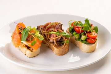 three types of bruschetta. With fish, meat, and veggie. Traditional Italian appetizers(bruschettas) on a white plate. Antipasti