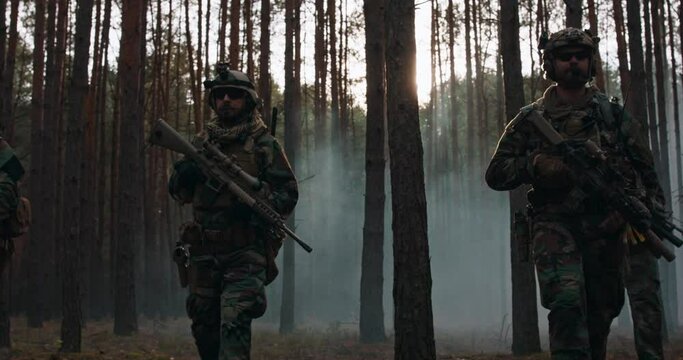 Fully equipped soldiers in camouflage uniform returning from action. A military operation, a unit walking in formation through a dark, thickly smoky forest