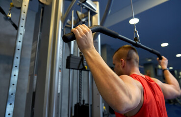 sport, fitness and bodybuilding concept - close up of man exercising with cable machine in gym