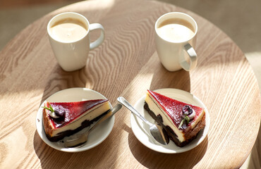 food, junk-food, culinary, baking and holidays concept - pieces of delicious cake on saucers with spoons and coffee cups on wooden table