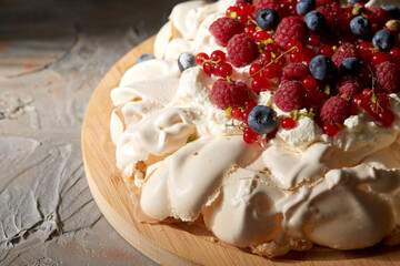 food, culinary, baking and cooking concept - close up of pavlova meringue cake decorated with berries on wooden serving board