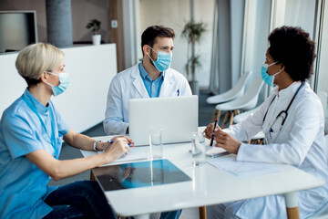 Obraz premium Group of healthcare experts with face masks talking during a meeting at medical clinic.
