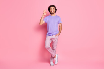Full length photo of guy arm pocket show okey toothy smile wear purple shirt pants footwear isolated pastel pink color background
