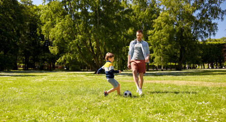 family, fatherhood and people concept - happy father and little son with ball playing soccer at summer park