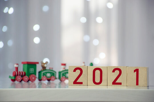 Coming soon New Year 2021 number on wooden cube block with colorful Christmas train and blurred bokeh lights on the background. Greeting card for winter holidays and Christmas.