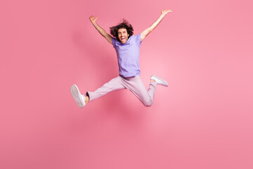 Fototapeta na wymiar Full size photo of energetic young man raise hands jump in air success wear pink pants isolated on pink color background