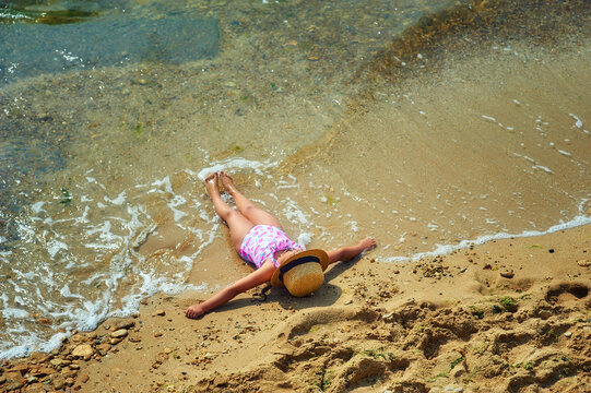A little girl sunbathes while lying on the sea coast. View from above