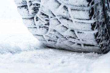 Car tire in the snow close up. Car tracks on the snow. Traces of the car in the snow. Winter tires. Tyres covered with snow at winter road. Winter road safety concept