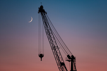 Suliet of the harbor crane on the background of the sky and the crescent moon