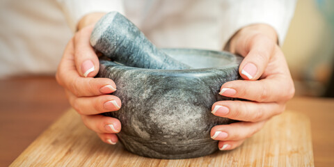 Mortar and pestle in the female hands on the cutting board