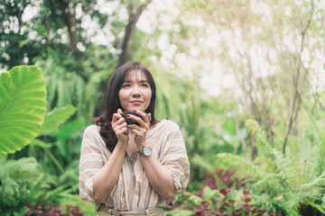 Young Asian woman relaxing in garden with a cup of coffee in a morning. A woman inhaled coffee