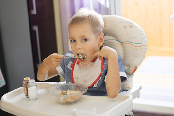 a boy with a bib eats porridge at the children's table