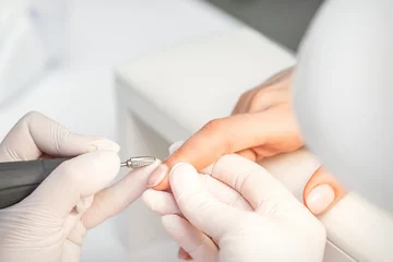 Foto auf Acrylglas Maniküre Maniküre entfernt Nagellack verwendet die elektrische Maschine der Nagelfeile während einer Maniküre