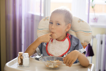 a boy with a bib eats porridge at the children's table