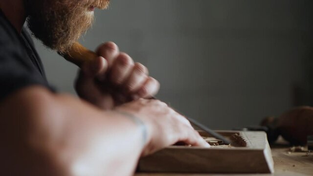 The craftsman processes the walnut board with a flat impact chisel. a woodcarver makes a wooden tray. woodcarver art.