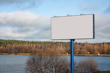 Horizontal landscape photo of a blank billboard on the foreground and calm lake with autumn forest on the background in cloudy day