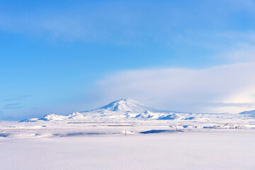 Fototapeta na wymiar Typical Icelandic winter landscape with mountains under the snow and blue sky. Beautiful winter landscape with mountains covered snow, cold frosty weather and white field in Iceland.