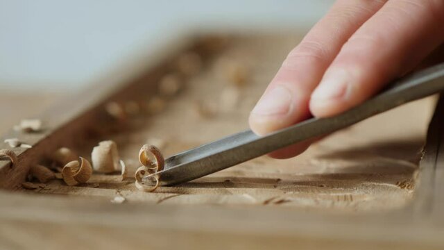 macro. a woodcarver processes a walnut wood board with a chisel. artisan makes a tea tray . vagatabon. tea tray.woodcarver art. the sound of carpentry tools