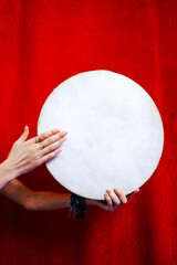A woman is holding and playing a tambourine with red background, only hands     