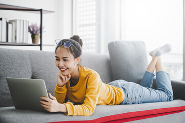 Beautiful young asian woman lying down and using computer laptop talking video conference call on...