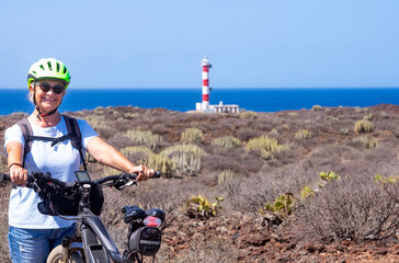 Happy senior woman with yellow helmet enjoying freedom and excursion with bicycle close to a...