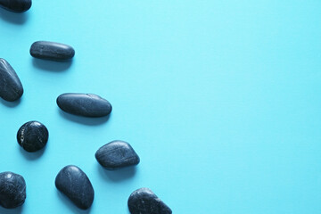 青い紙の背景に置いた黒い小石のグループ。平置きの俯瞰撮影。
