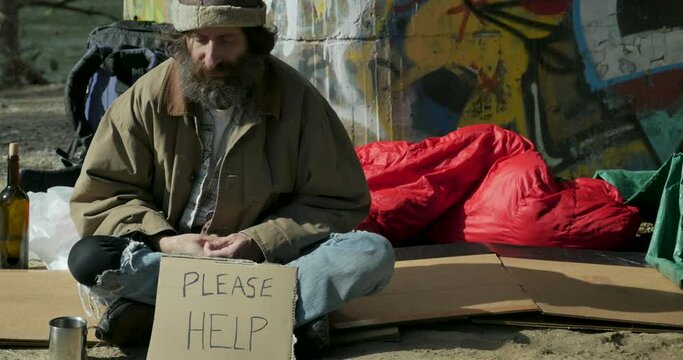 Homeless man sitting outside with a please help sign in front of him