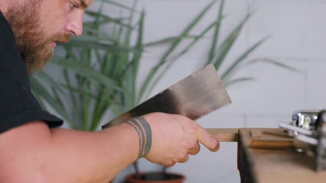 a woodworker with beard carves a dovetail joint on an oak board with a Japanese hand saw for wood.handmade carpentry. the sound of carpentry tools