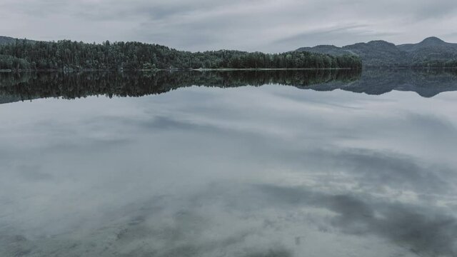 Calm mountain lake and reflection of the clouds moving over the lake. Fishes jumping