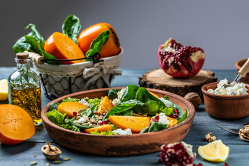 Fototapeta na wymiar Persimmon salad with spinach, nuts, goat cheese, pomegranate, pumpkin seeds. Healthy vegetarian food concept