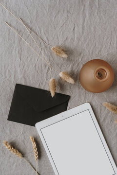 Flatlay Of Blank Screen Tablet Pad, Fluffy Pom Pom Plants, Rye / Wheat Ear Stalks, Envelope On Grey Washed Linen Background. Home Office Desk Workspace. Business, Work Template. Flat Lay, Top View.