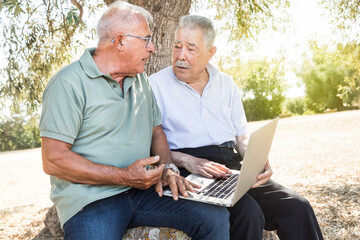 Coppia di amici discute seduti in un parco davanti a un computer portatile 