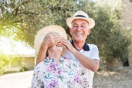 marito e moglie anziani con il cappello  si divertono in un contesto naturale: Lui chiude gli occhi a lei divertito.