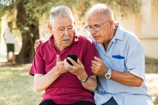 Due vecchi amici scherzano e ridono davanti a uno smartphone seduti in un parco natura