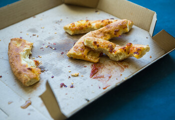 Leftover pizza pieces laying on the pizza box carton. Fast food garbage in the food court.