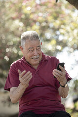 Naklejka na ściany i meble Anziano sorridente che fa una videochiamata con il suo smartphone in un parco all'aria aperta