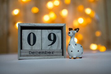 Cube wooden calendar showing date on 9th December with ceramic reindeer figurine over bokeh...