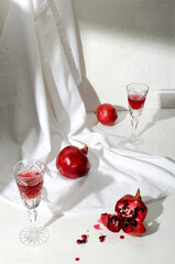 Vertical image.Fresh ripe pomegranates, glasses full of pomegranate alcohol drink on the white desk against bright wall
