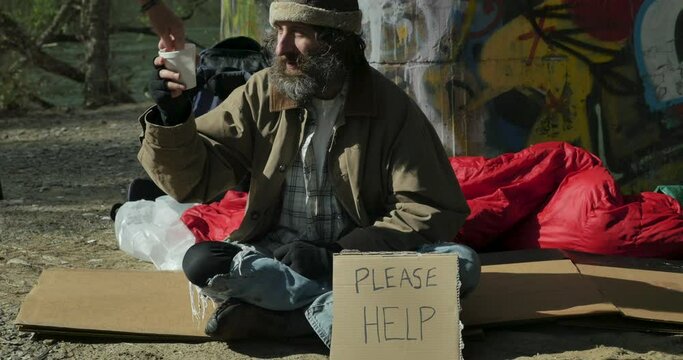 Homeless man with a styrofoam cup begging for money from a woman on the street